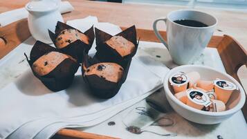A tray with muffins in paper cups, a cup of coffee, and a bowl of coffee creamer.
