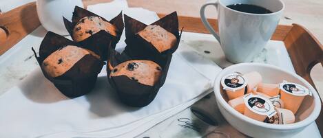 A tray with muffins in paper cups, a cup of coffee, and a bowl of coffee creamer.