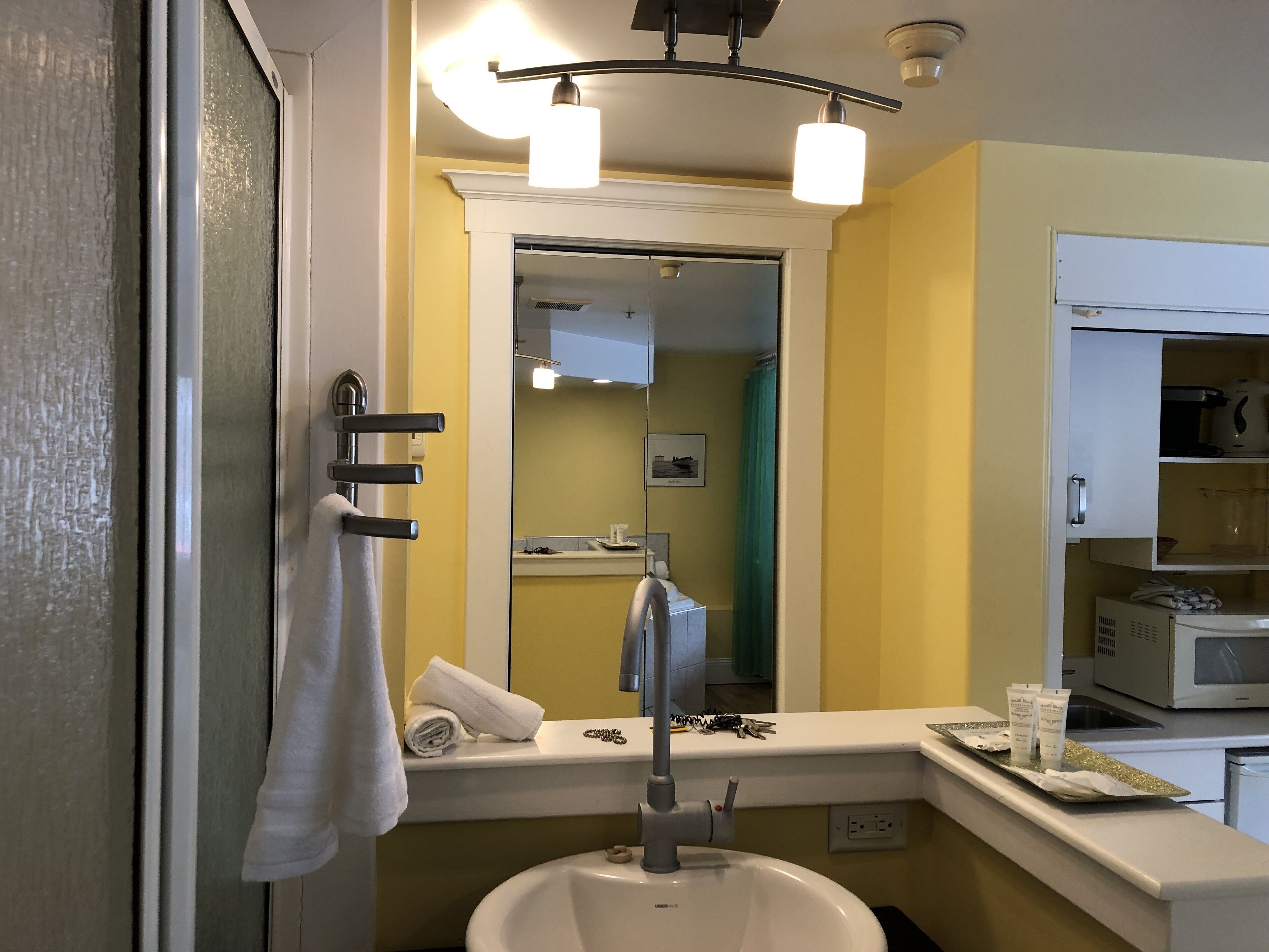 A bathroom with a sink, mirror, towel rack, and a microwave on the countertop.