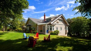Ein Haus mit einem gepflegten Rasen, zwei Adirondack-Stühlen und blauem Himmel.