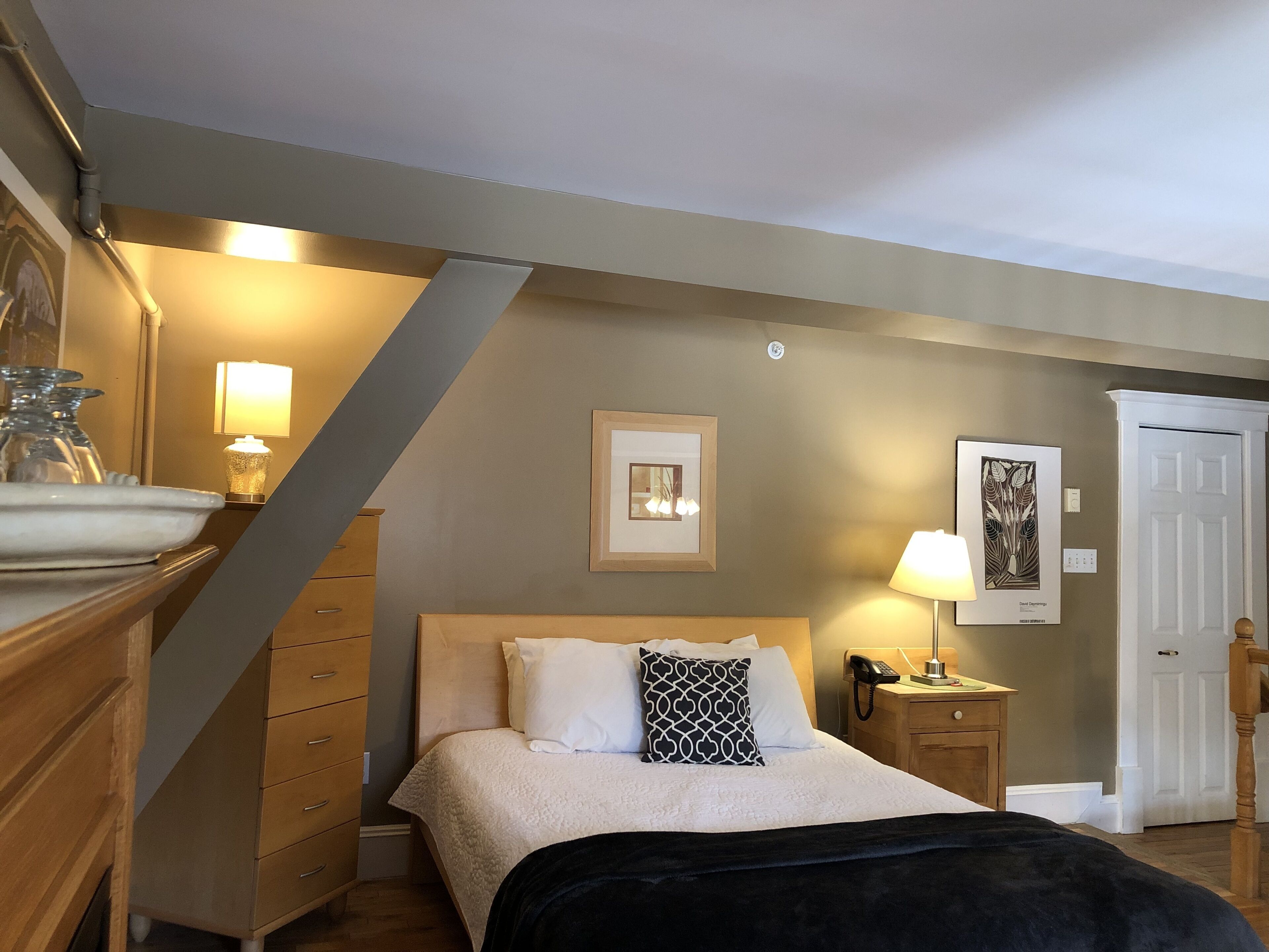 Een slaapkamer met een bed, nachtkastjes, een lamp, een lijst met een afbeelding en een deur.