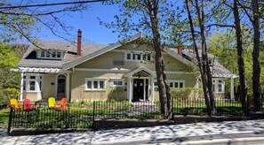A two-story house with a front porch, a chimney, and a fenced yard with colorful chairs. - Leaside Manor by The Leaside Group (St. John's)