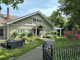 A two-story house with a front porch, a covered entryway, and a small garden with various plants and flowers.