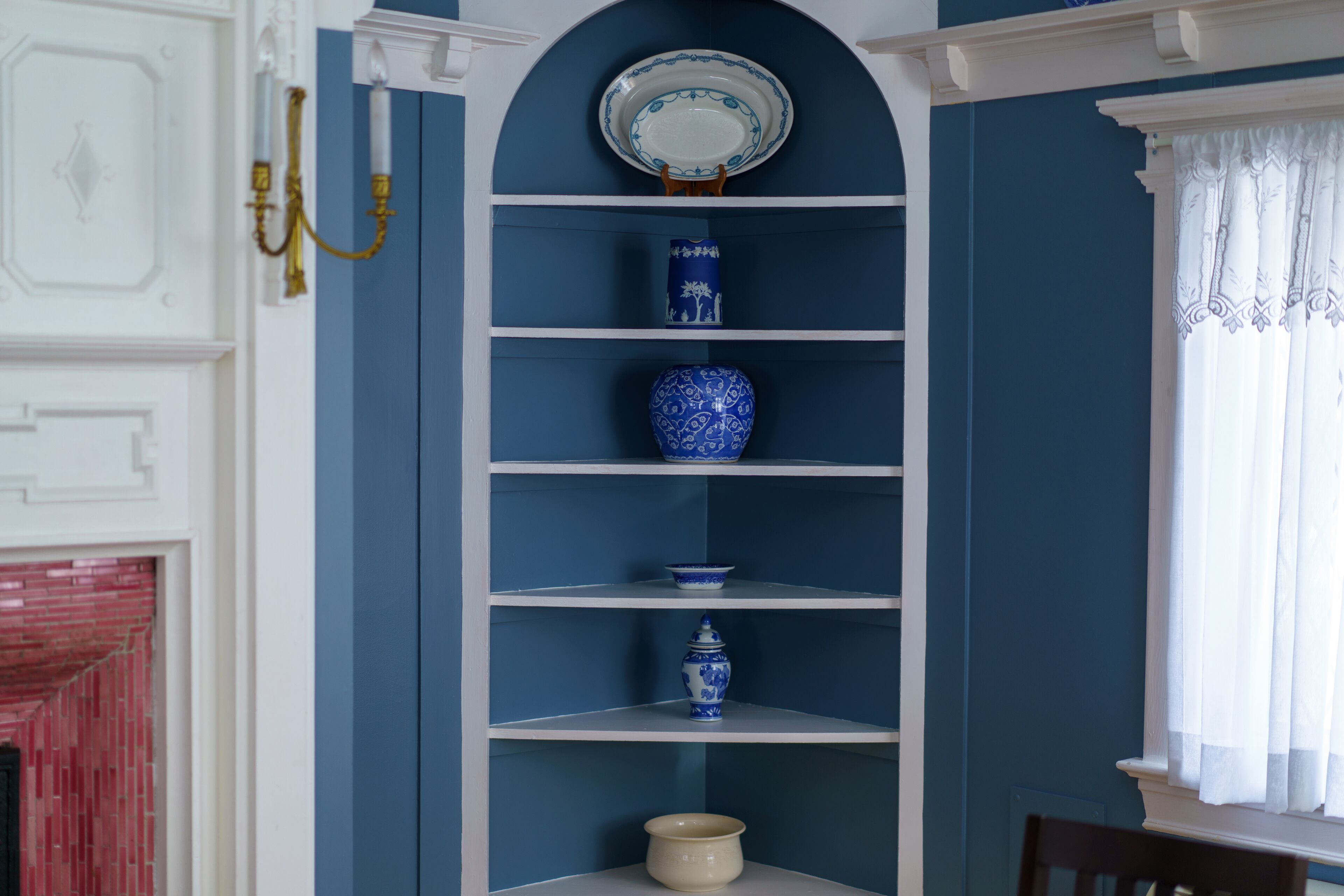 A room with a blue wall, white shelves, and a white fireplace.