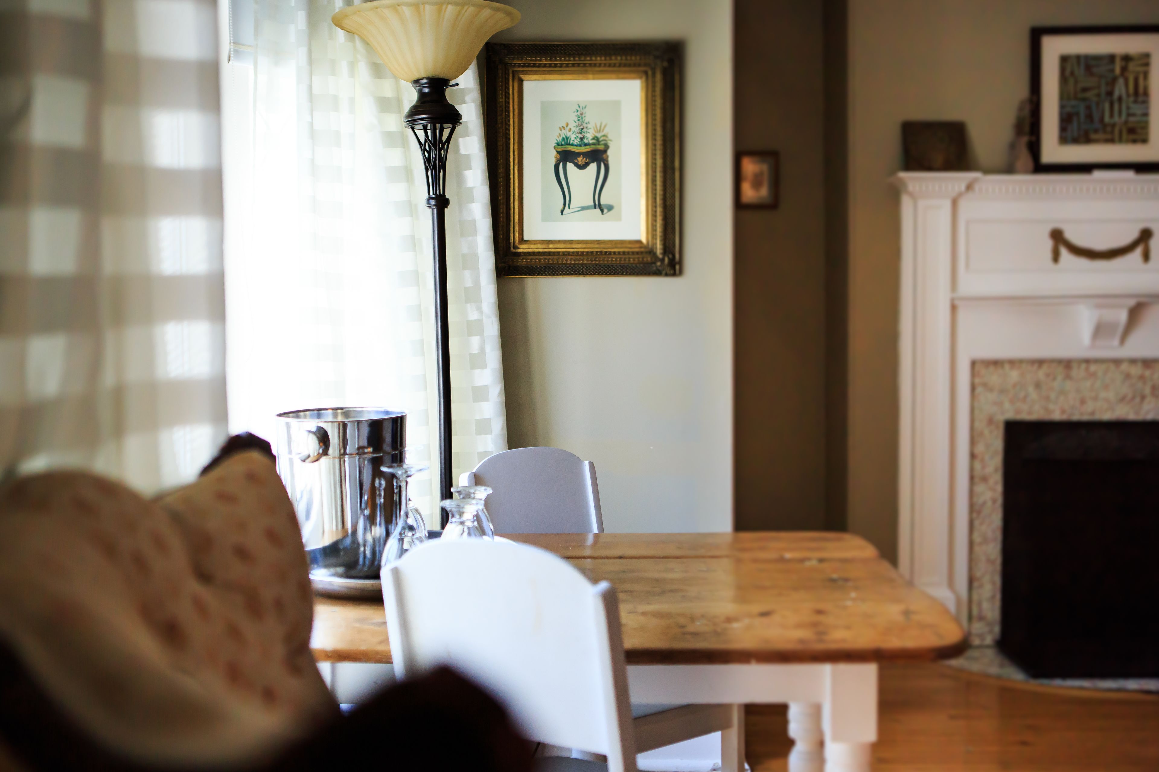 Een eethoek met een houten tafel, witte stoelen, een metalen karaf en een lamp.