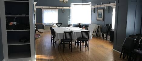A spacious dining area with a large table and chairs, a chandelier, and a view of the outdoors through large windows.
