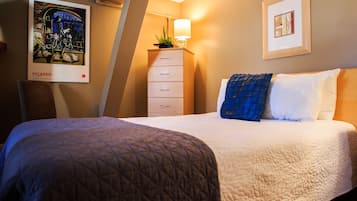 Une chambre d’hôtel avec un lit, une commode, une lampe et deux tableaux encadrés au mur.