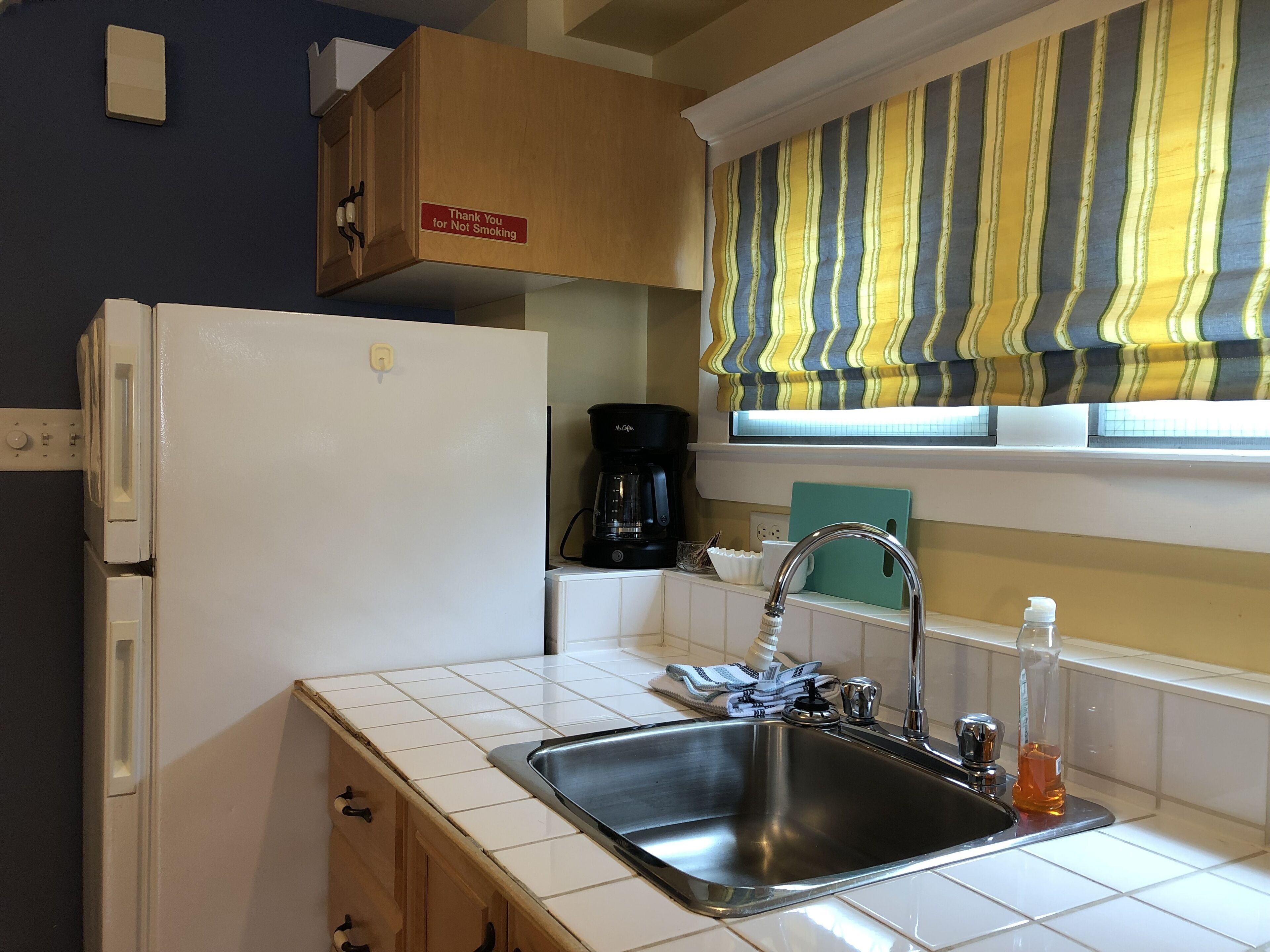 A kitchen with a stainless steel sink, a coffee maker, and a refrigerator.