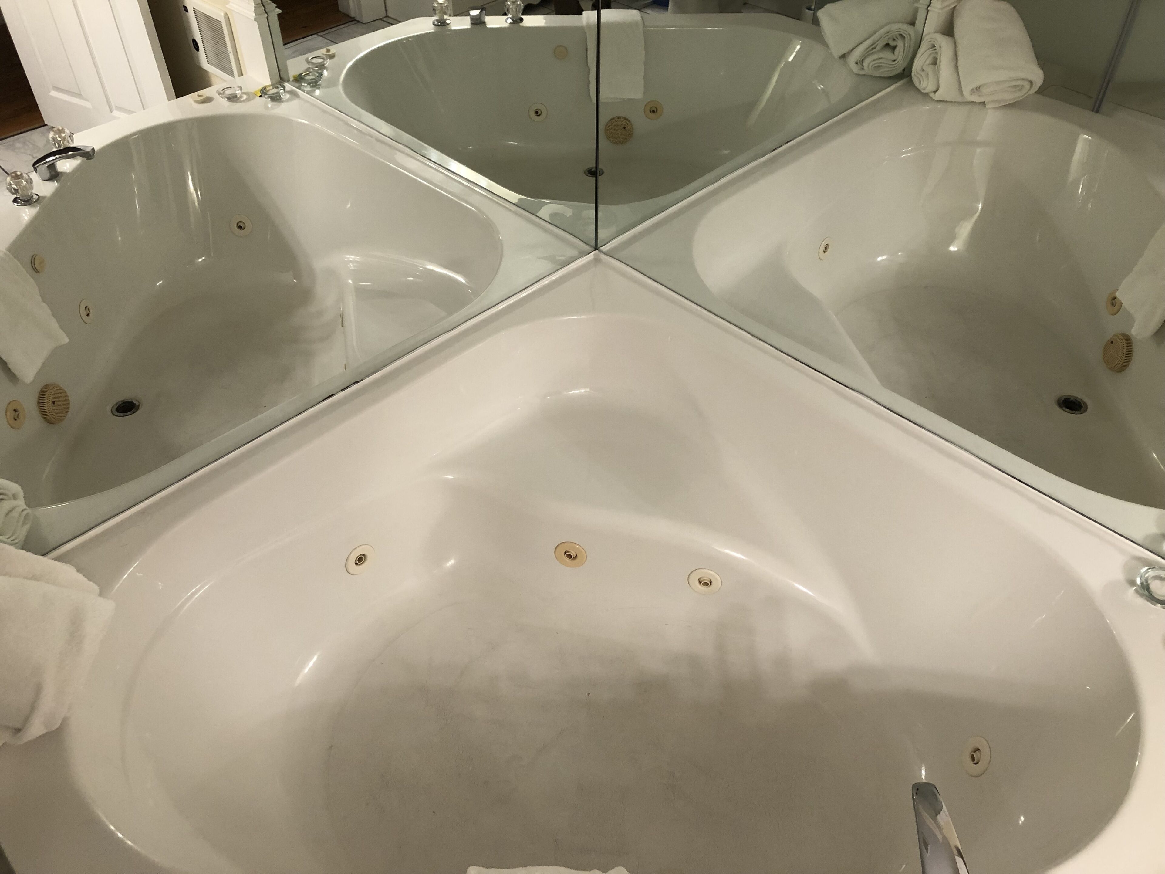 A large, oval-shaped bathtub with a glass partition, surrounded by white tiles and a mirror reflecting the room.