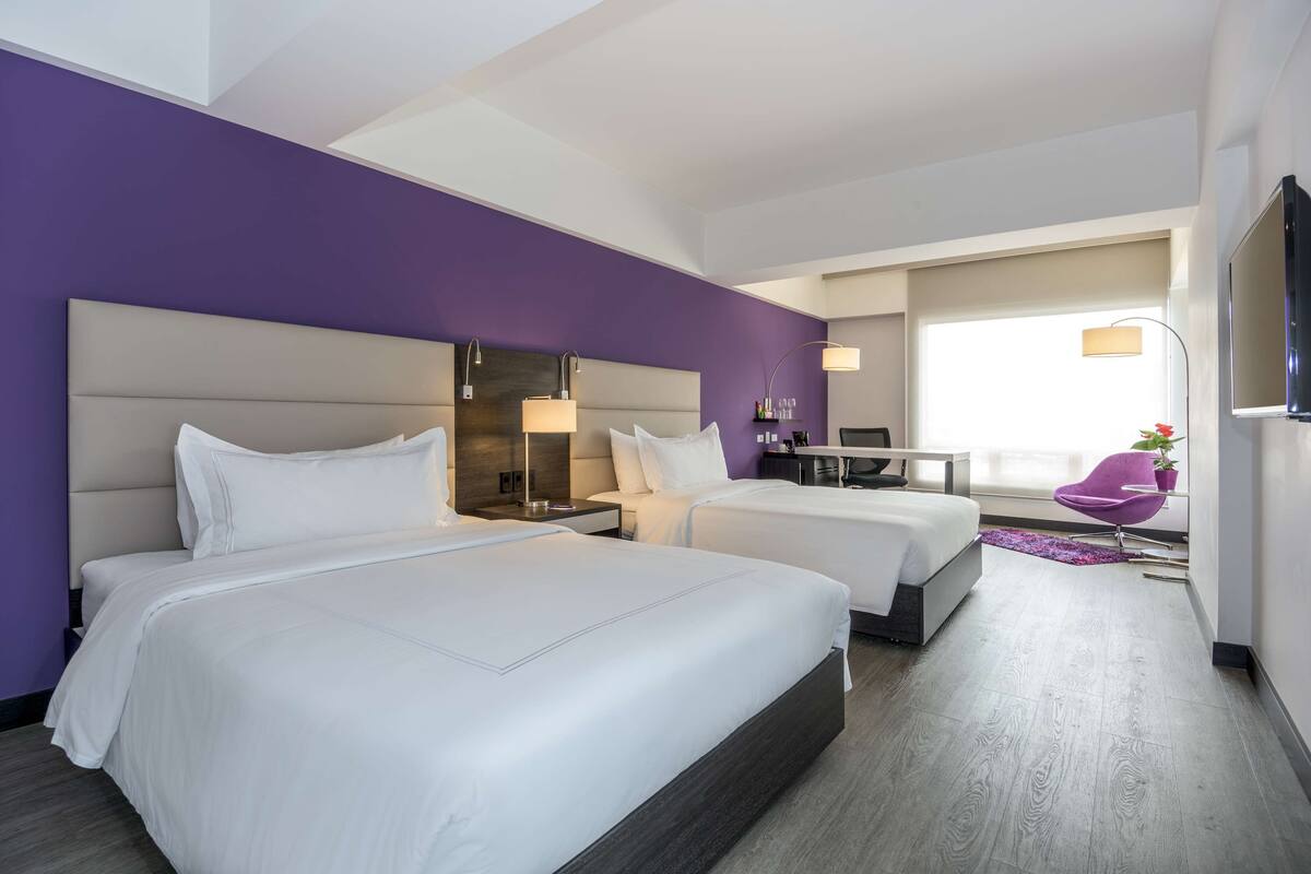 Una habitación de hotel con dos camas, un escritorio, una silla y un televisor.