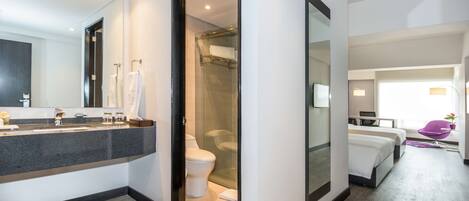 A modern hotel room with a bathroom featuring a glass shower enclosure, a large mirror, and a vanity with a dark countertop.