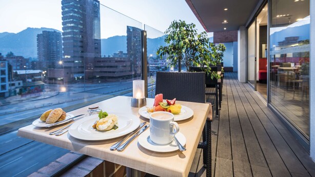 Un balcón con una mesa lista para el desayuno, que incluye cruasanes, huevos y fruta.