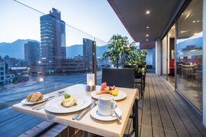 A balcony with a table set for breakfast, including croissants, eggs, and fruit.