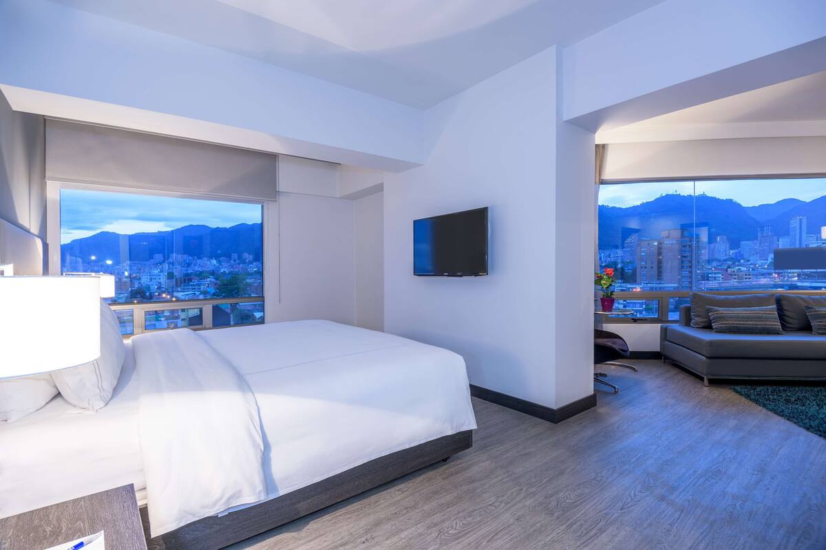 Una habitación de hotel moderna con una cama grande, televisión de pantalla plana y un balcón con vistas a la ciudad.