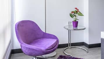 A corner room with a purple chair, a small table with a potted plant, a tall floor lamp, and a purple rug.