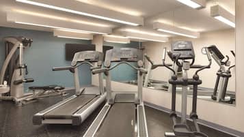 Un gimnasio con cintas de correr, elípticas y un espejo grande.