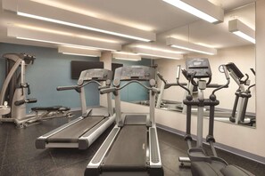 A gym with treadmills, elliptical machines, and a mirrored wall.