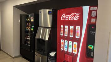 Uma área de máquinas de venda automática, incluindo uma máquina de Coca-Cola, um bebedouro e uma máquina de snacks.
