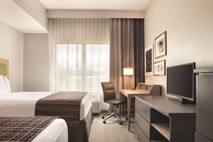 Habitación de hotel con cama, escritorio, silla, televisión y ventana con cortinas.