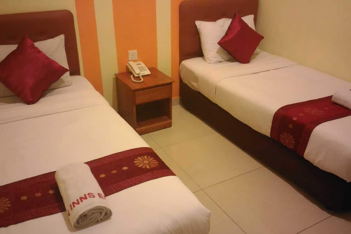 Dos camas individuales con ropa de cama roja y blanca, una mesita de noche de madera con un teléfono y una toalla estampada en rojo y blanco sobre el suelo.