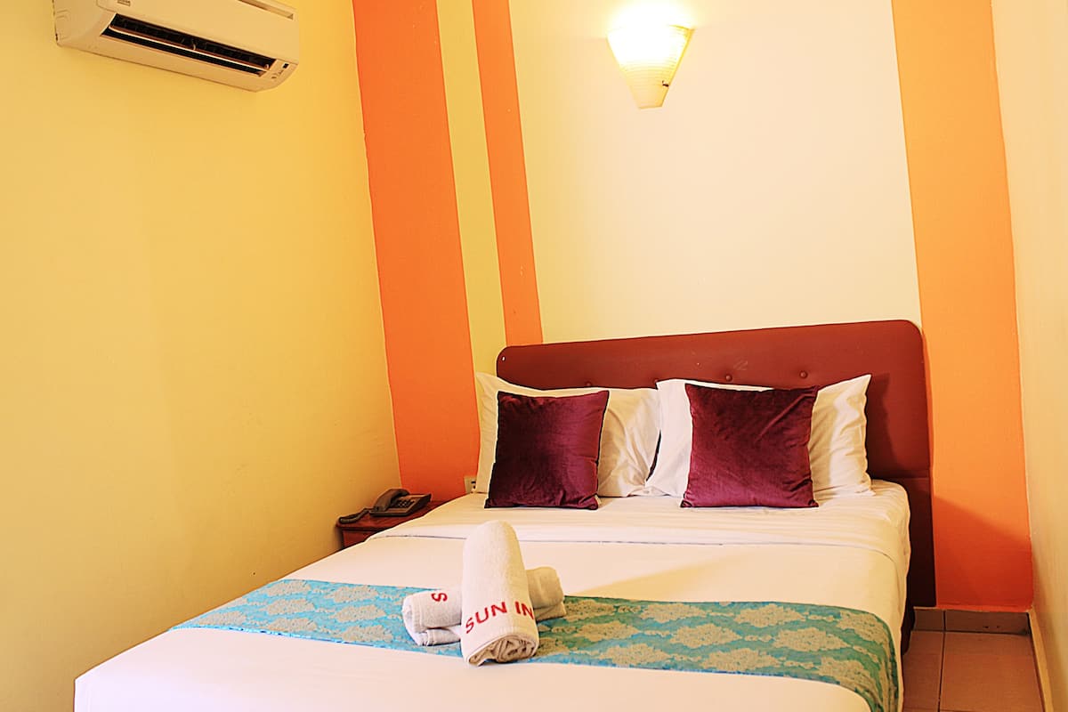 Una habitación de hotel con cama, mesita de noche, teléfono y aire acondicionado instalado en la pared.