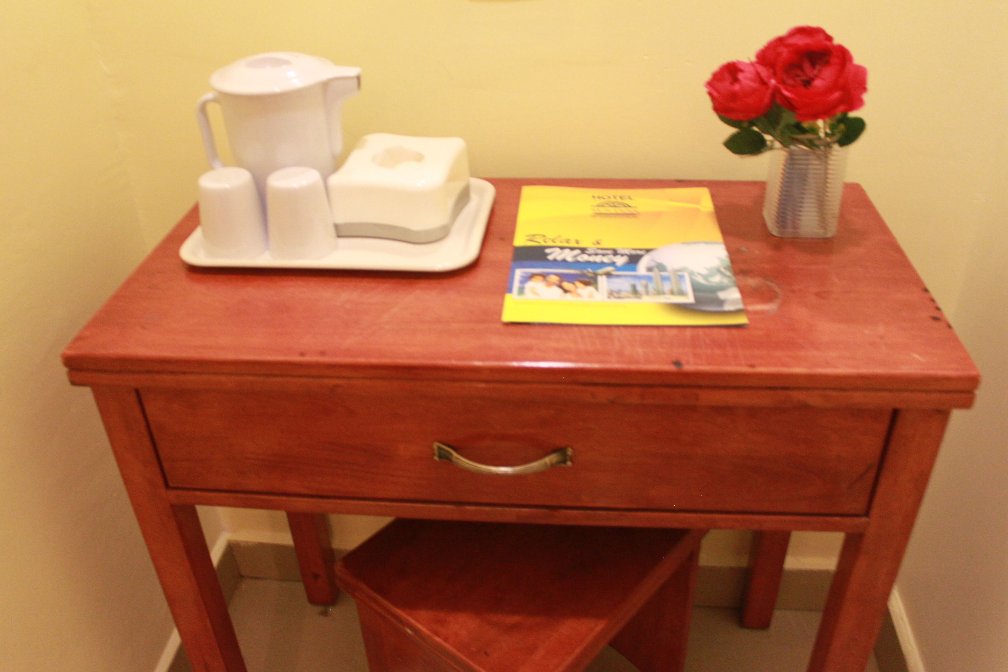 Une table de chevet en bois, sur laquelle se trouvent une machine à café blanche, une boîte de mouchoirs et un magazine.