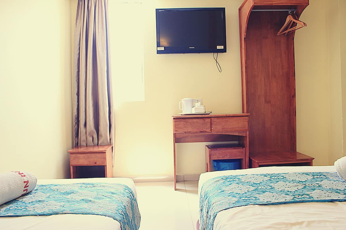 Una habitación de hotel con dos camas, un escritorio de madera, un televisor y un armario.