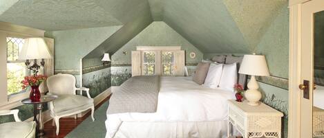 A bedroom with a high ceiling, a bed, a chair, a nightstand, and a window with a view.