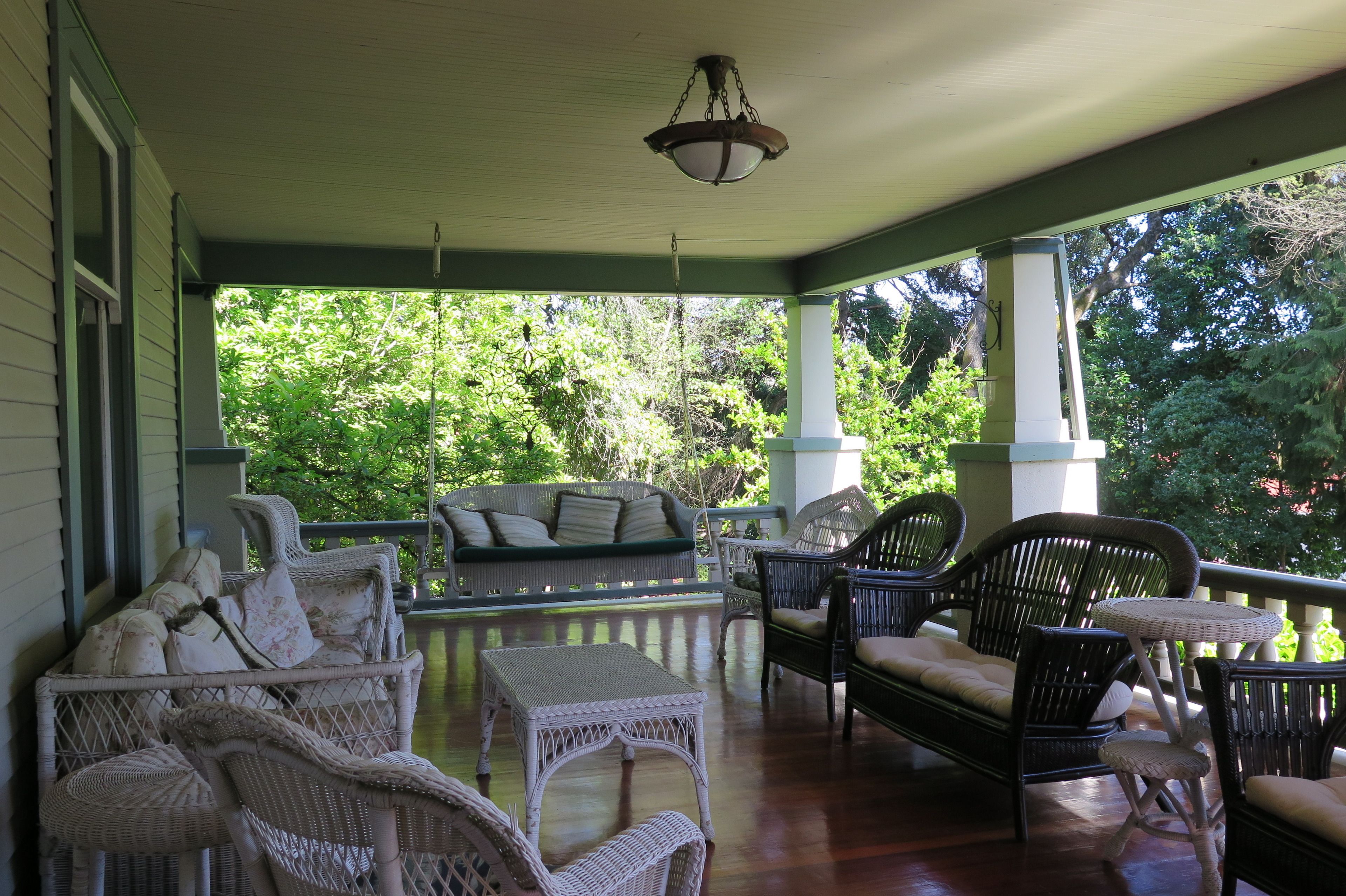 A covered porch with wicker furniture, a table, and a hanging light fixture.