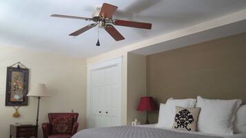Une chambre d’hôtel avec un lit, un fauteuil rouge, un ventilateur de plafond, une porte blanche et un tableau encadré au mur.