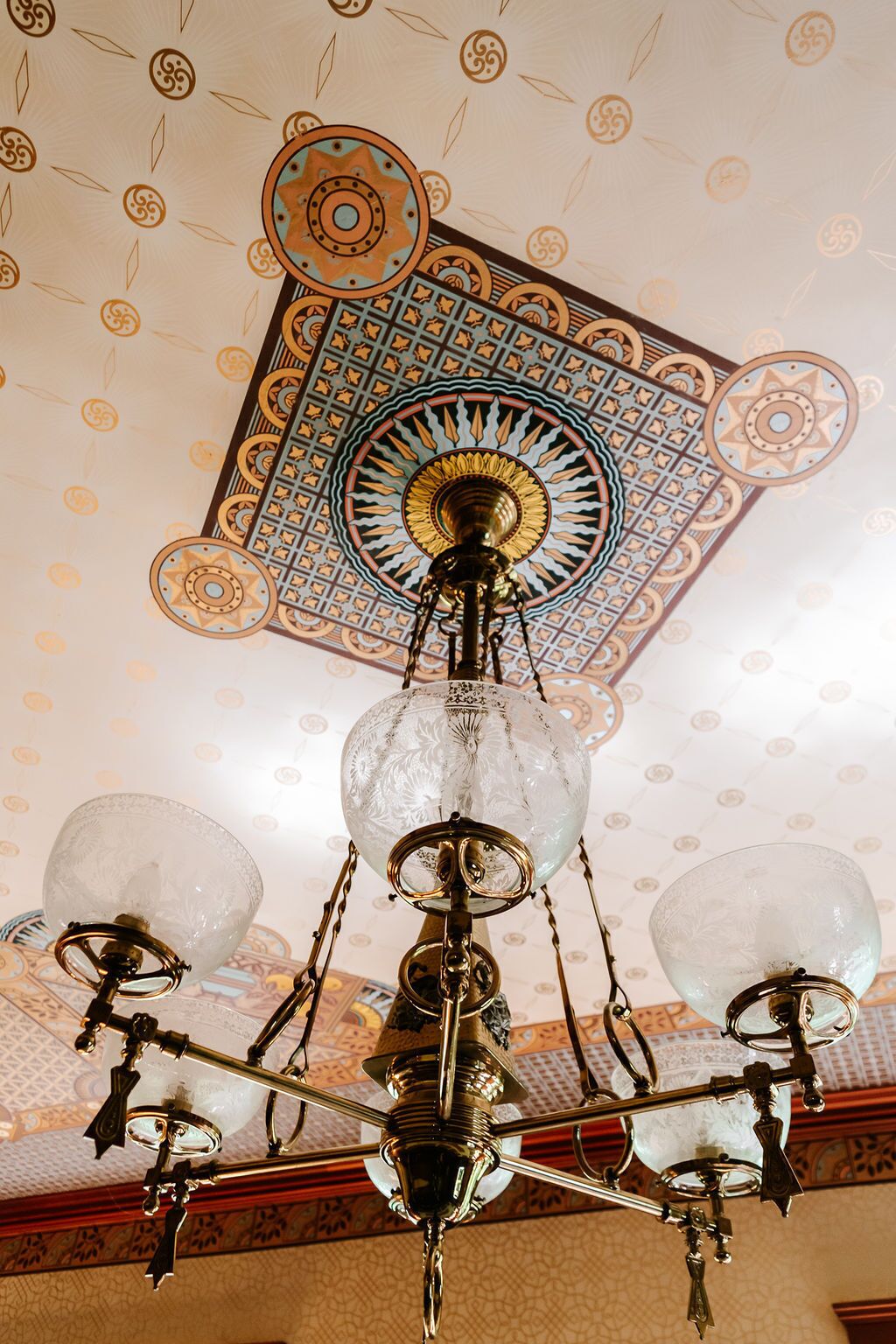 A chandelier with three glass globes and a decorative ceiling with geometric patterns.