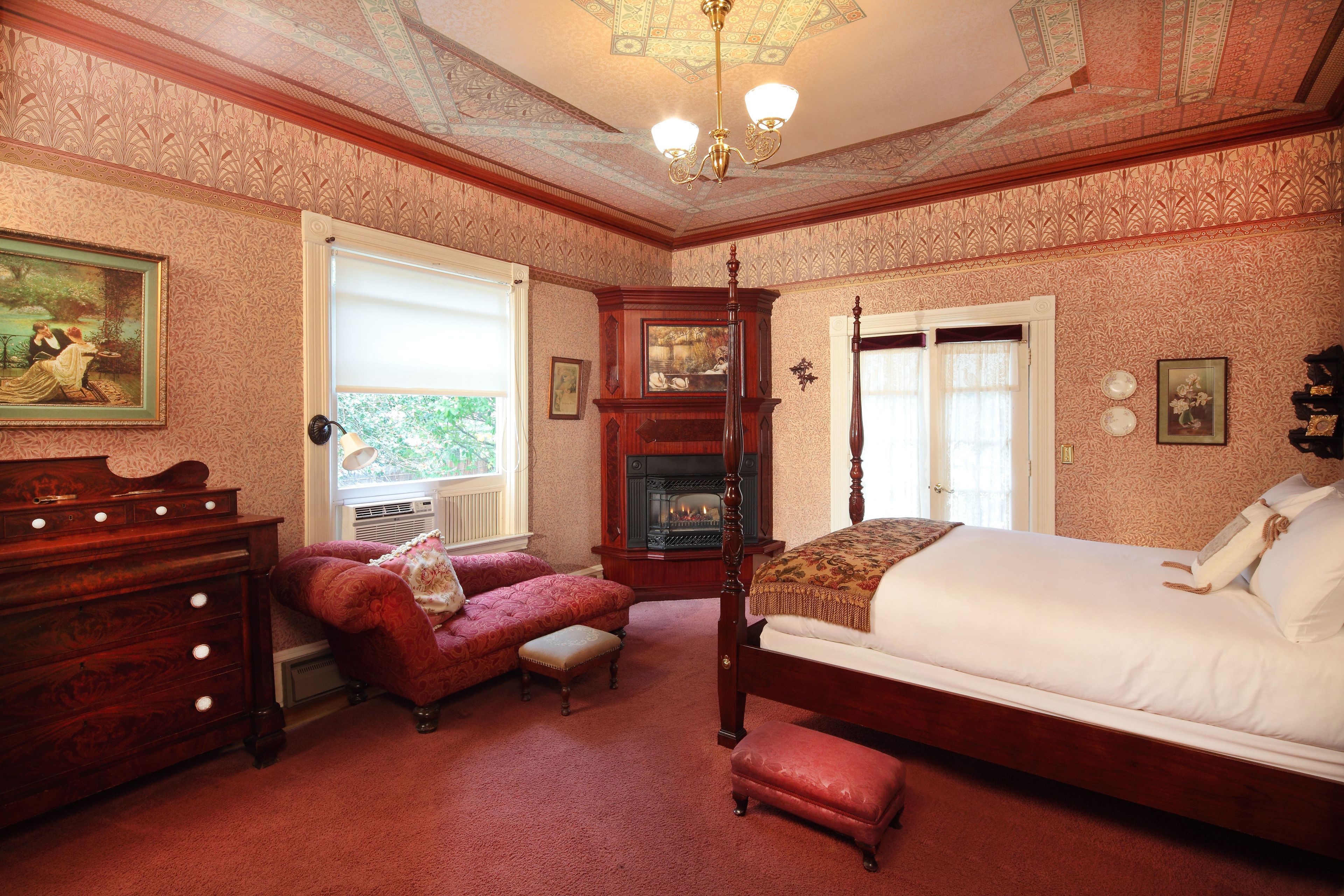 A traditional bedroom with a four-poster bed, a fireplace, and a red upholstered sofa.
