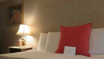 A hotel room with a bed, a nightstand with a lamp, a painting on the wall, and a welcome card on the bed.