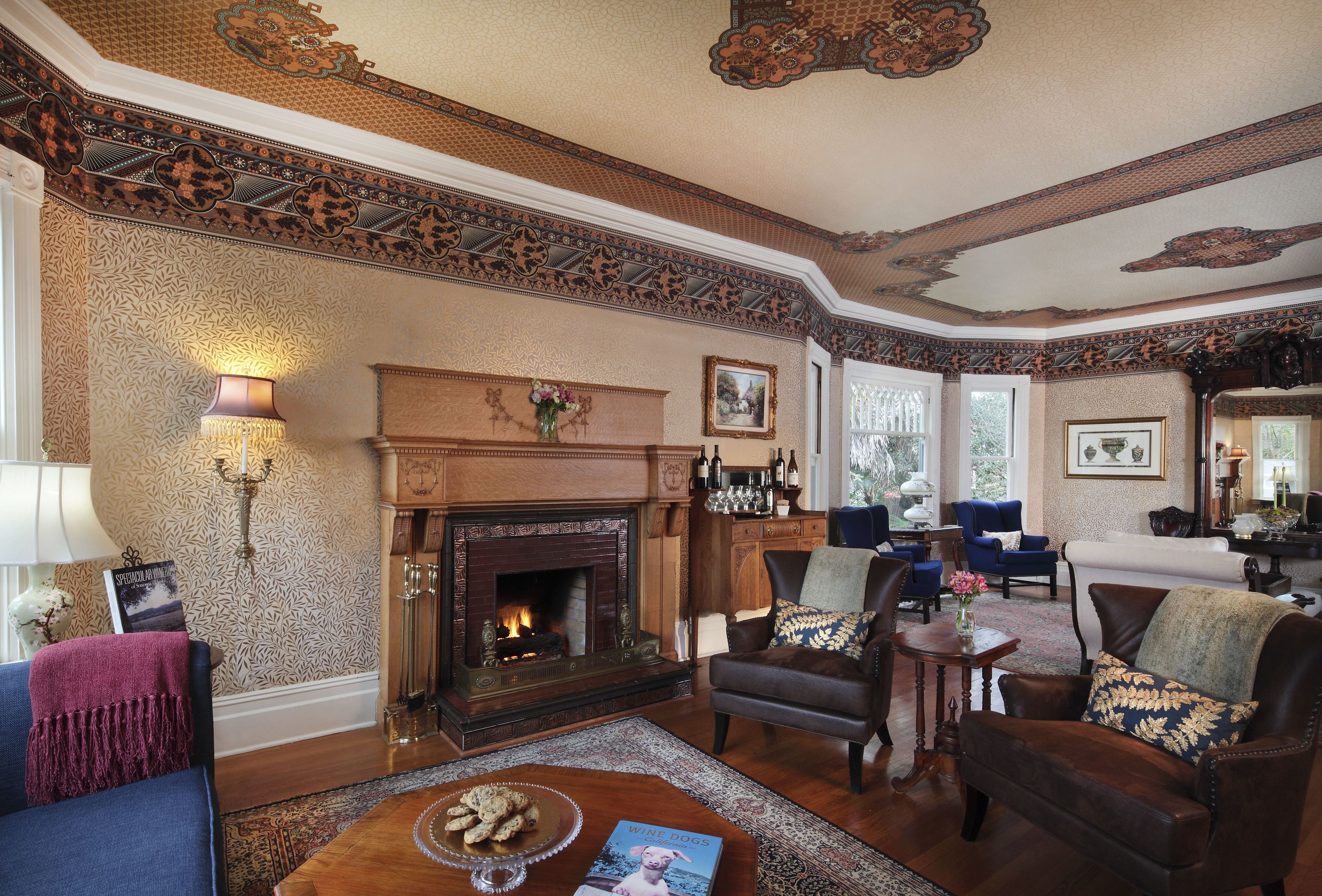 A traditional living room with a fireplace, patterned wallpaper, and classic furniture.