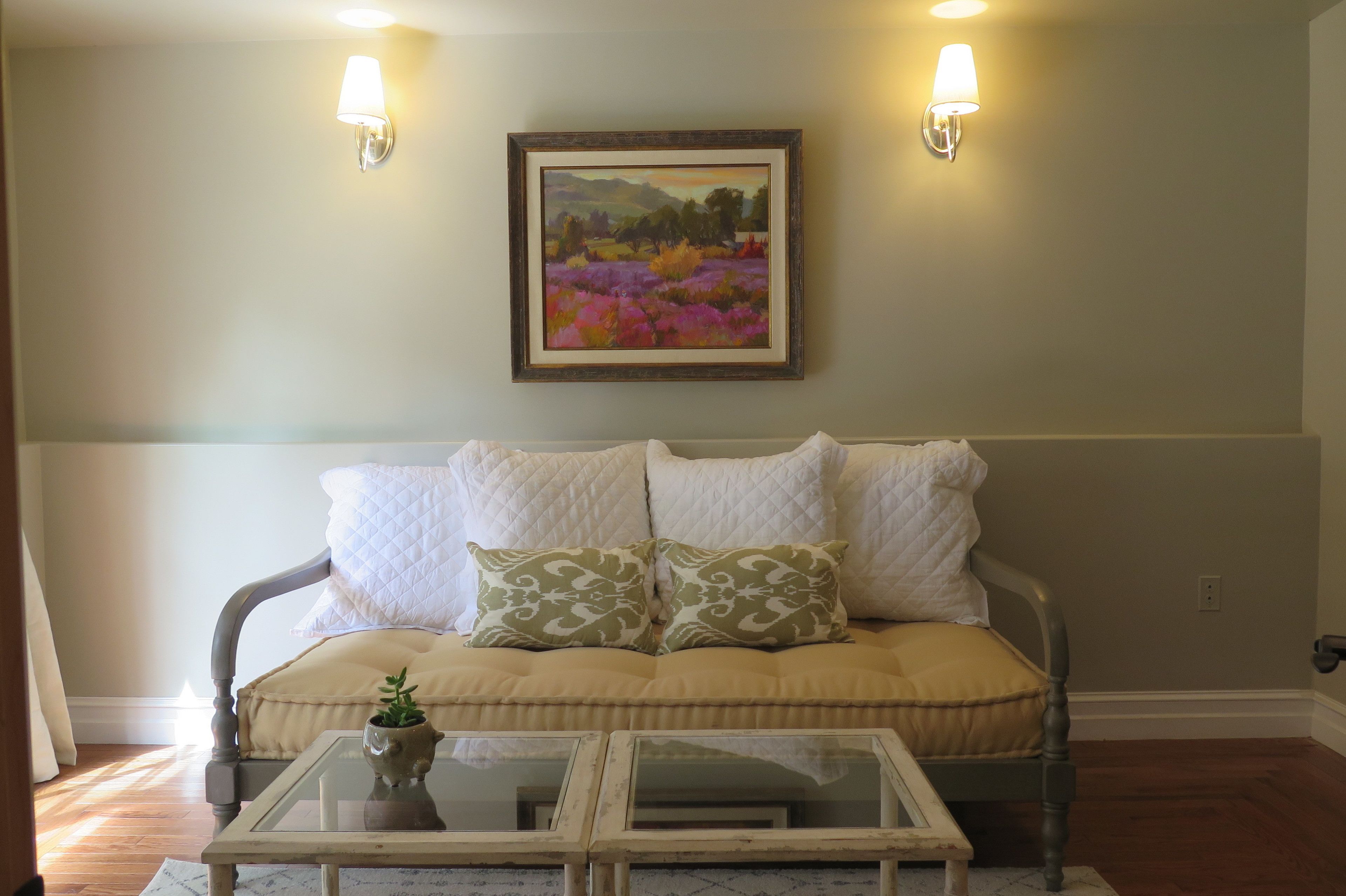 A living room with a beige sofa, two wall-mounted lamps, and a framed landscape painting.