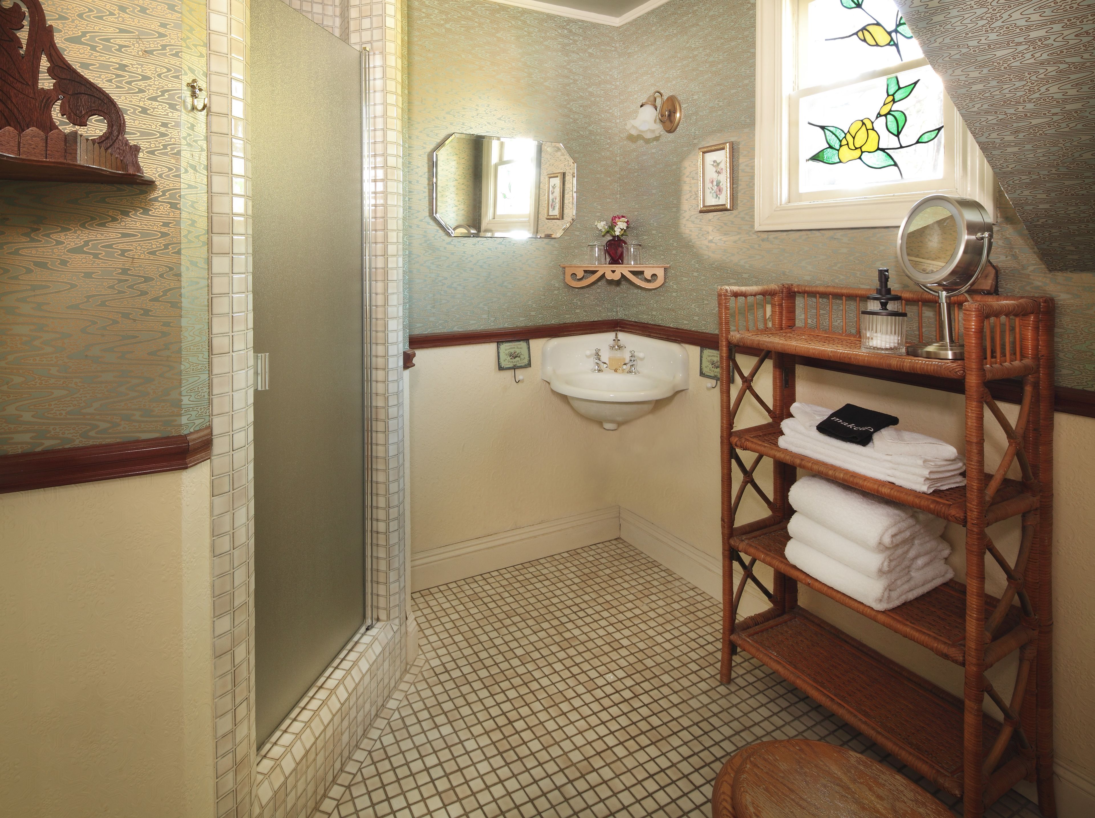 A bathroom with a shower, a sink, a mirror, and a wicker shelf with towels.