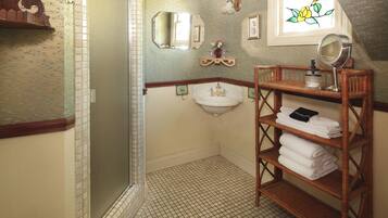 A bathroom with a shower, a sink, a mirror, and a wicker shelf with towels.
