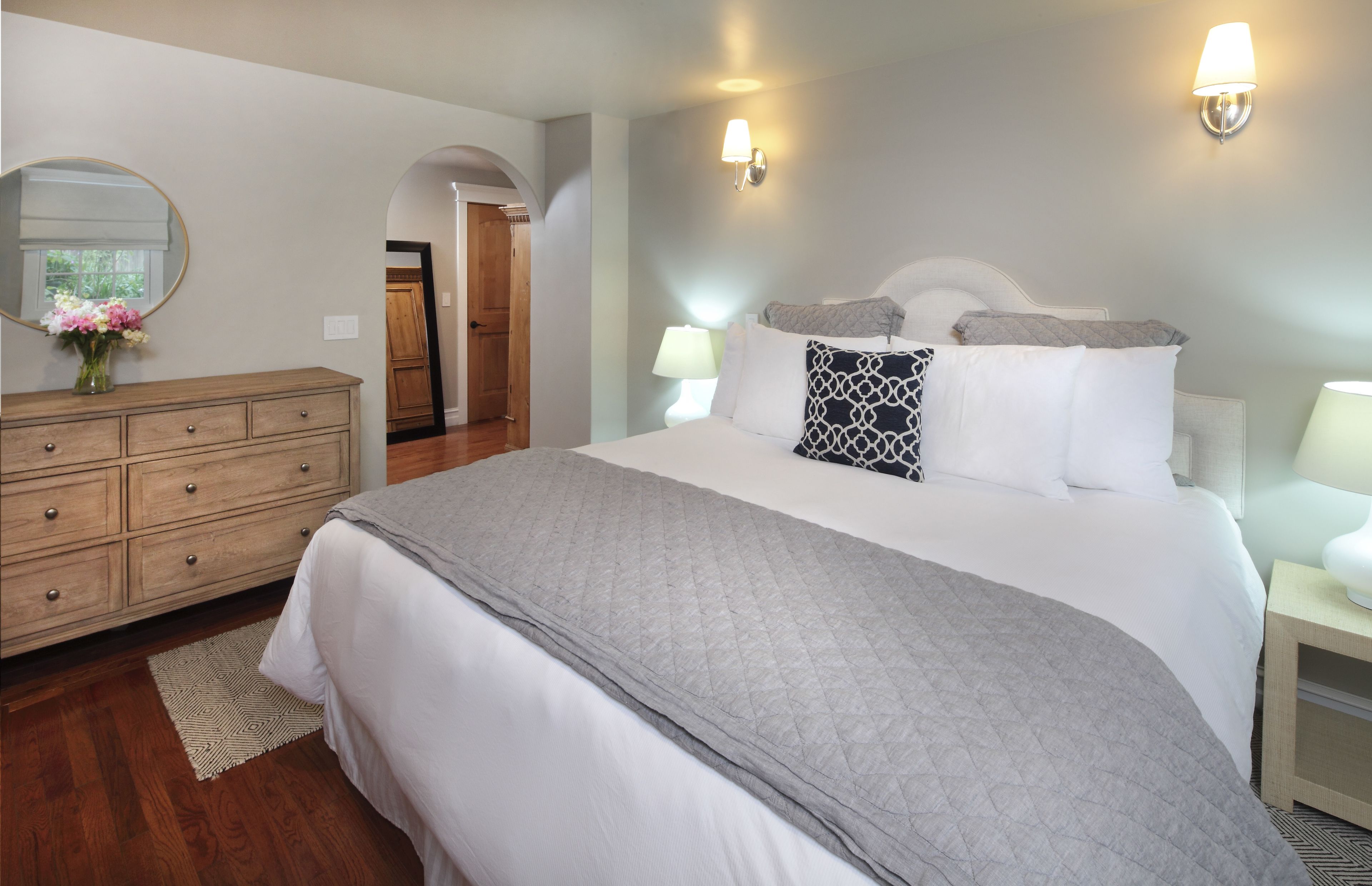 A neatly arranged bedroom with a large bed, a dresser, and a mirror.
