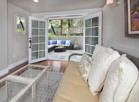Una sala de estar acogedora con un sofá blanco, una mesa de centro de vidrio y vistas a un patio trasero con zona de estar.