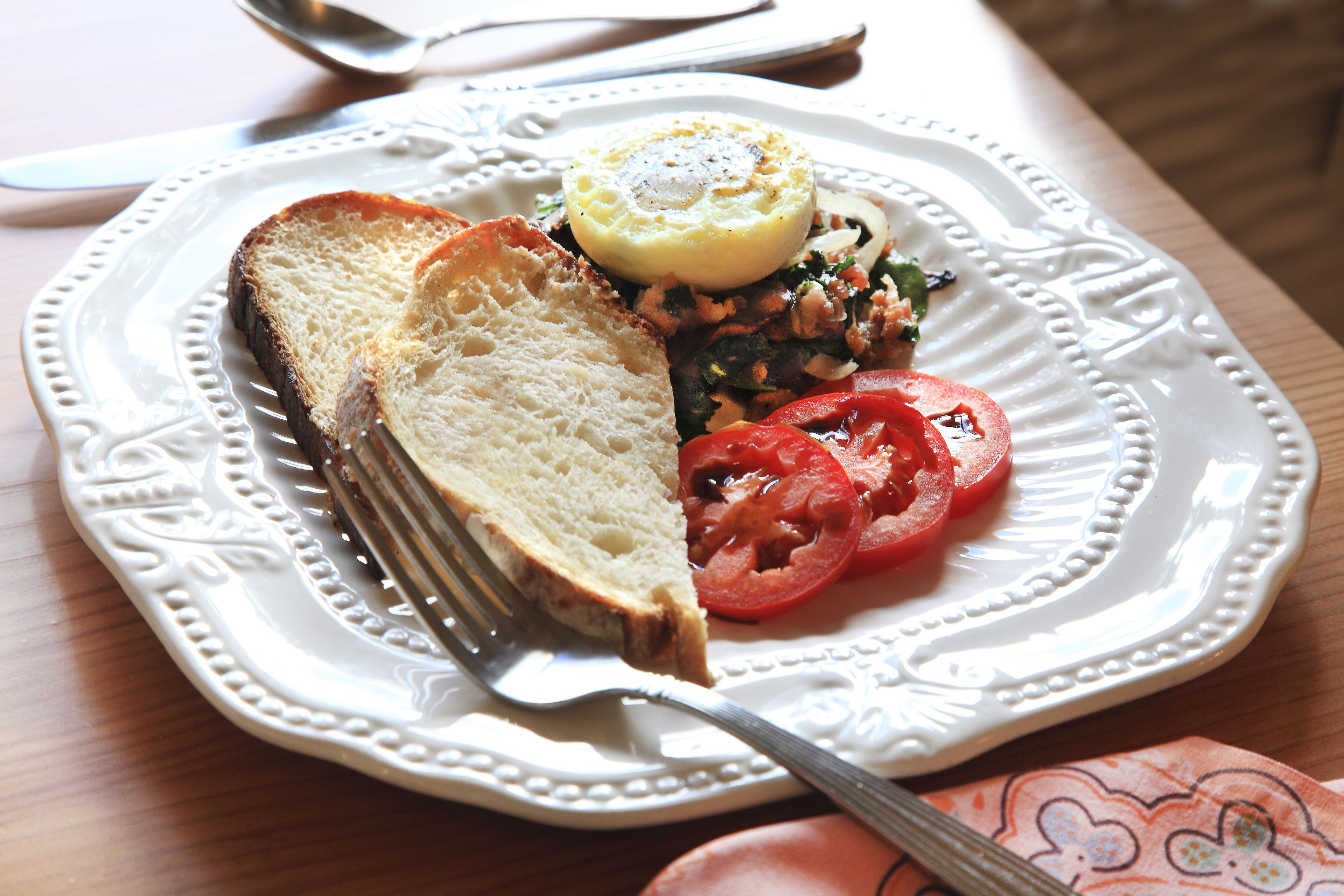 A plate with a slice of bread, a tomato slice, and a small egg on a decorative plate.