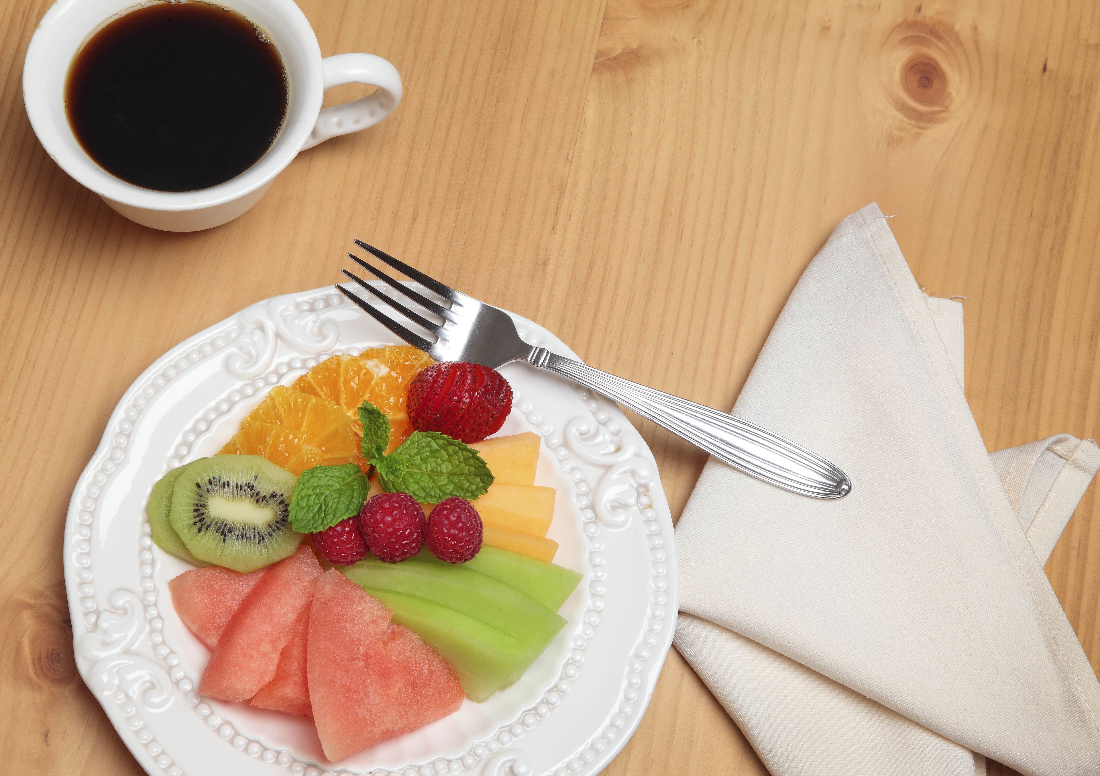 A white plate with a variety of fruits and a cup of coffee on a wooden table.