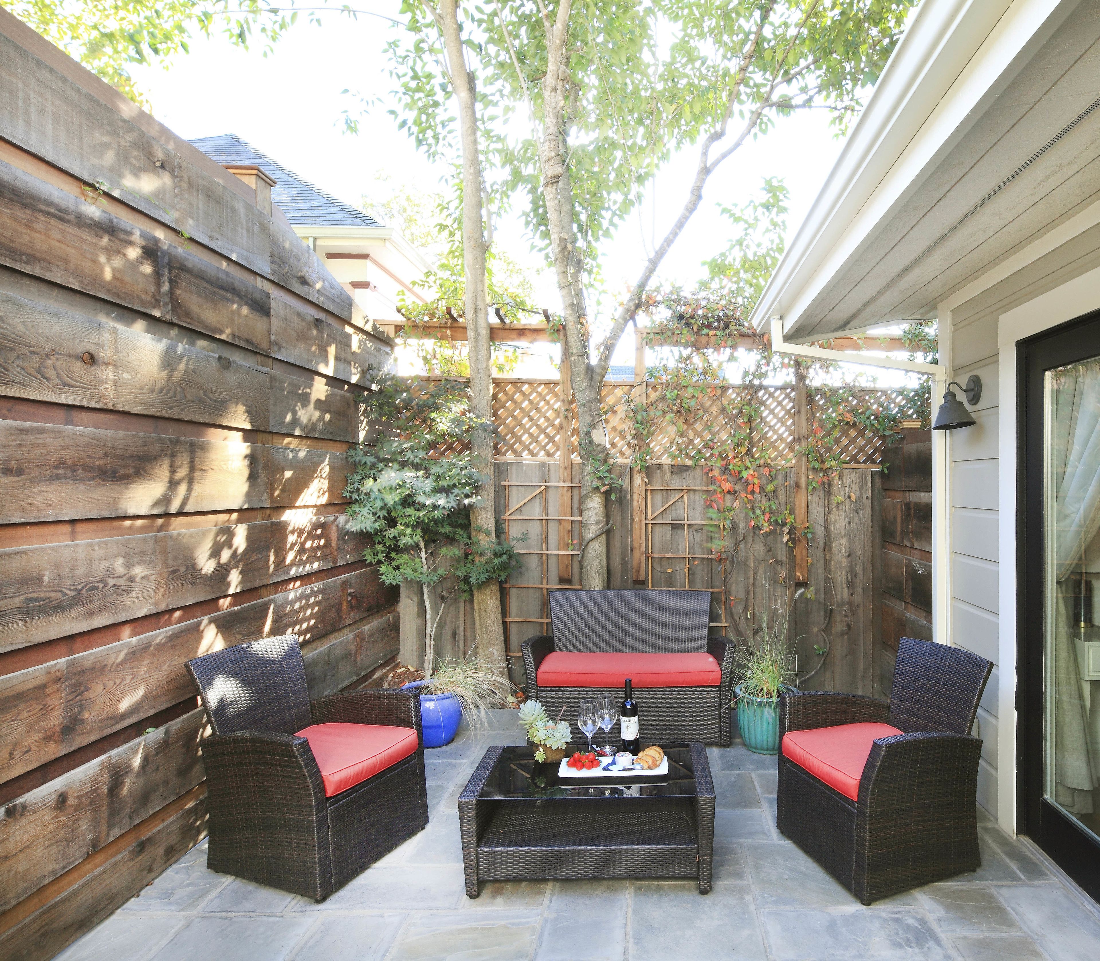 A patio area with wicker furniture, a table with a tray of food and drinks, and a wooden fence.