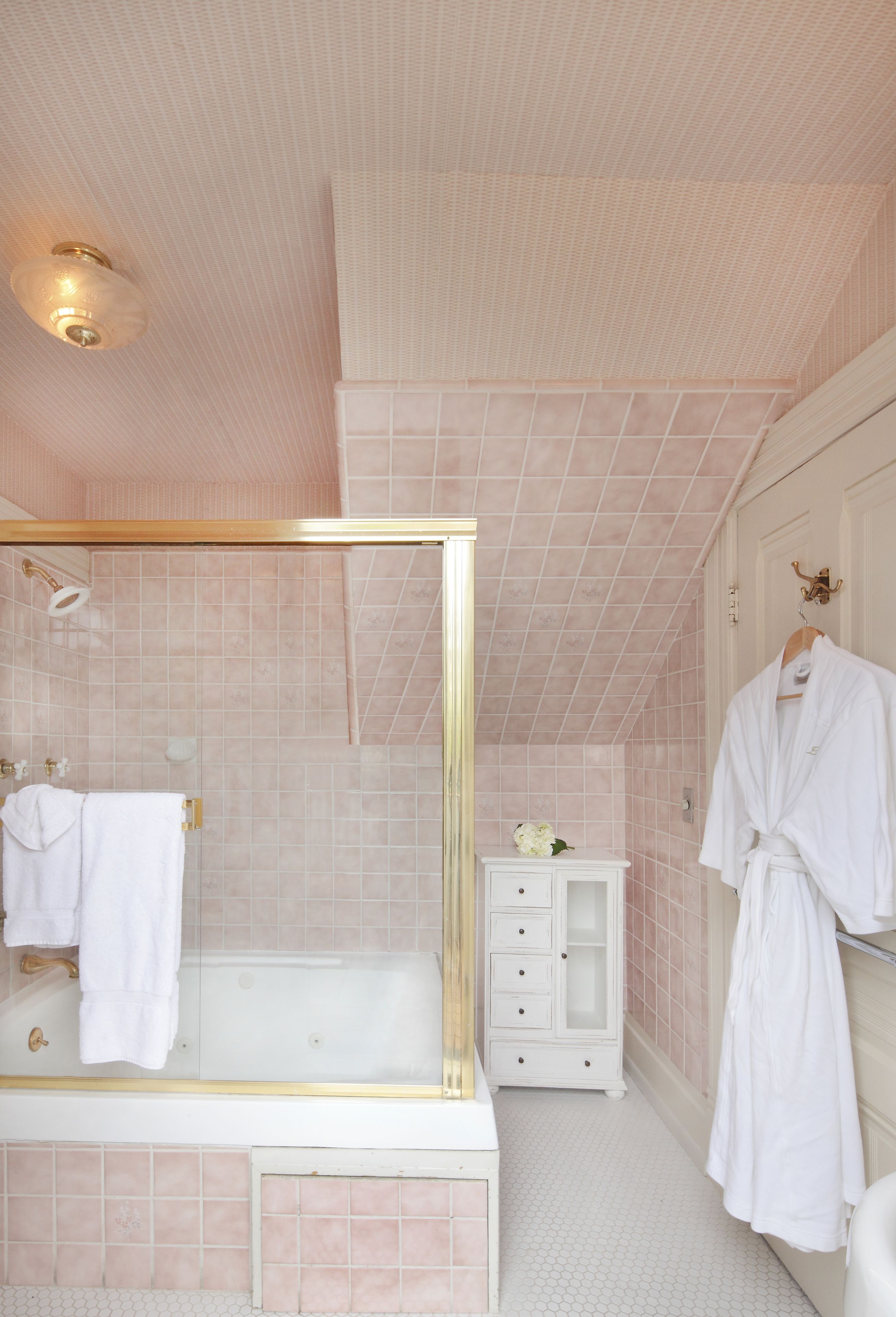 Une salle de bain dotée d’une douche à parois de verre, d’un meuble-lavabo blanc avec des tiroirs et d’un peignoir accroché au mur.