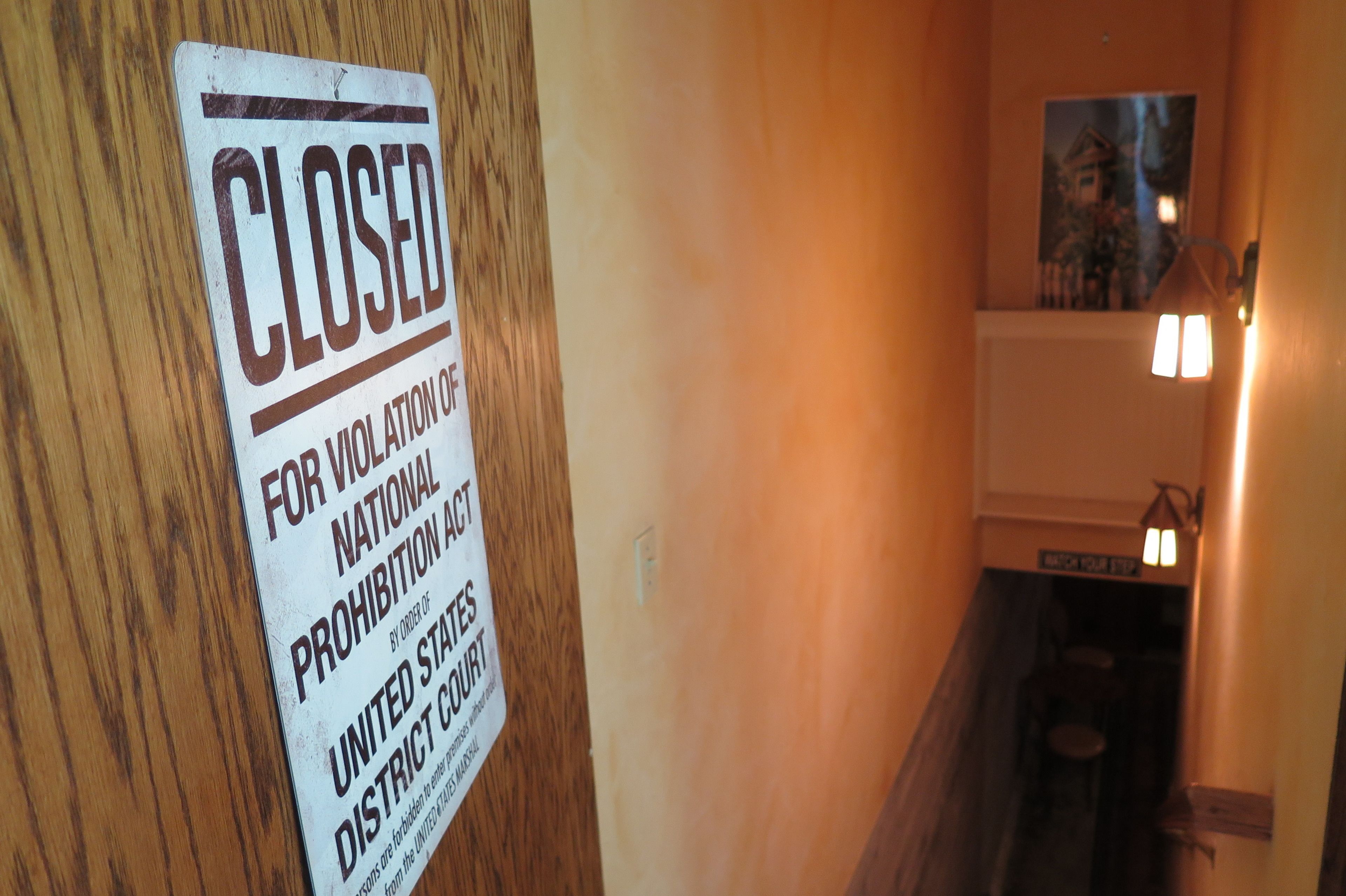 A closed sign on a wooden door, a staircase, and a wall-mounted light fixture.