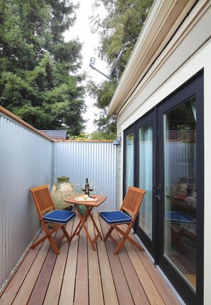An outdoor patio with a wooden deck, two wooden chairs, a table, and a large vase.