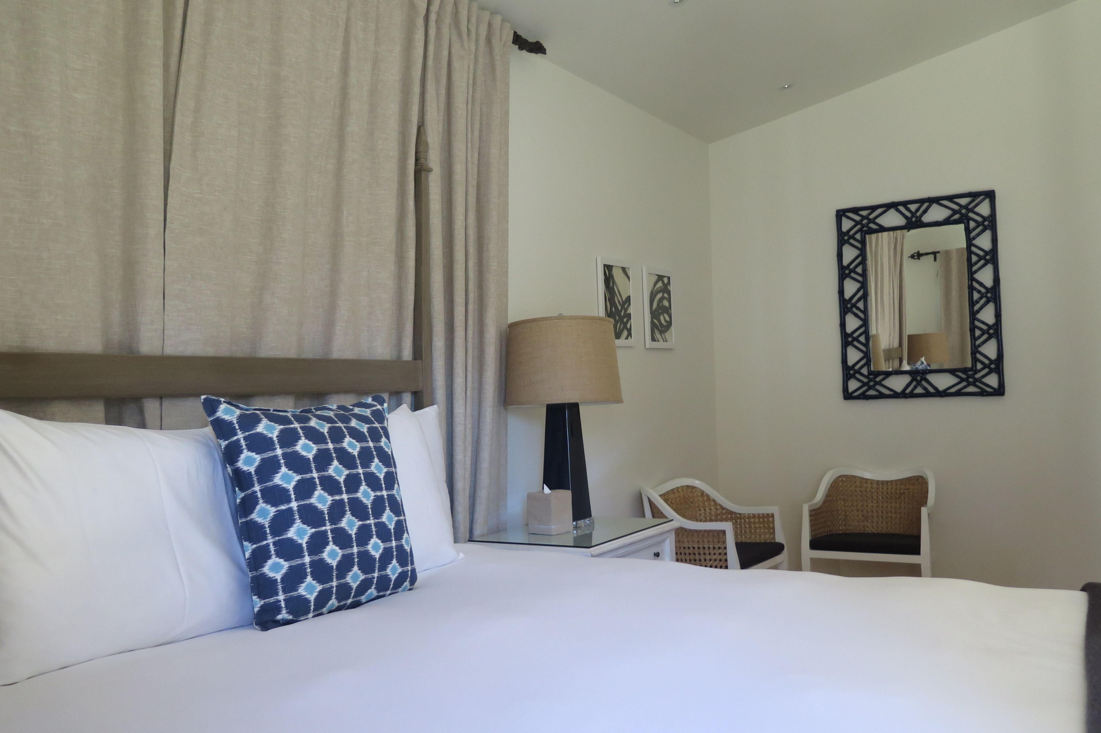 Una habitación de hotel con una cama, una mesita de noche, una lámpara, dos sillas y un espejo en la pared.