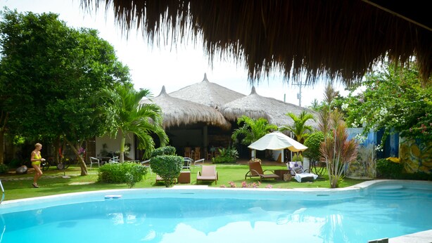 A swimming pool with a thatched-roof structure in the background, surrounded by greenery and outdoor seating. - Vanilla Sky Dive Resort (Panglao)