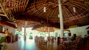 A spacious indoor area with a high ceiling and thatched roof structures. There are multiple wooden tables and chairs arranged for dining. - Vanilla Sky Dive Resort (Panglao)