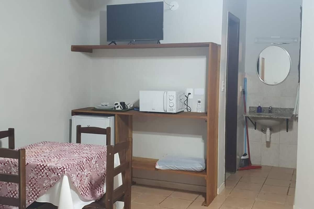 Une petite pièce comprenant un lit, un bureau avec un ordinateur, un téléviseur fixé au mur, un four à micro-ondes et un évier.