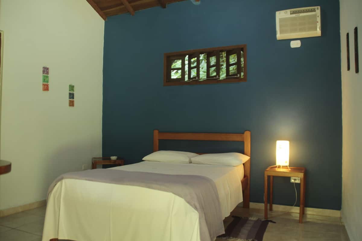 Une chambre à coucher comprenant un lit, une table de chevet et un climatiseur fixé au mur.